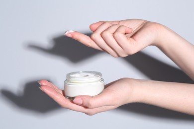 Woman with jar of cream on grey background, closeup