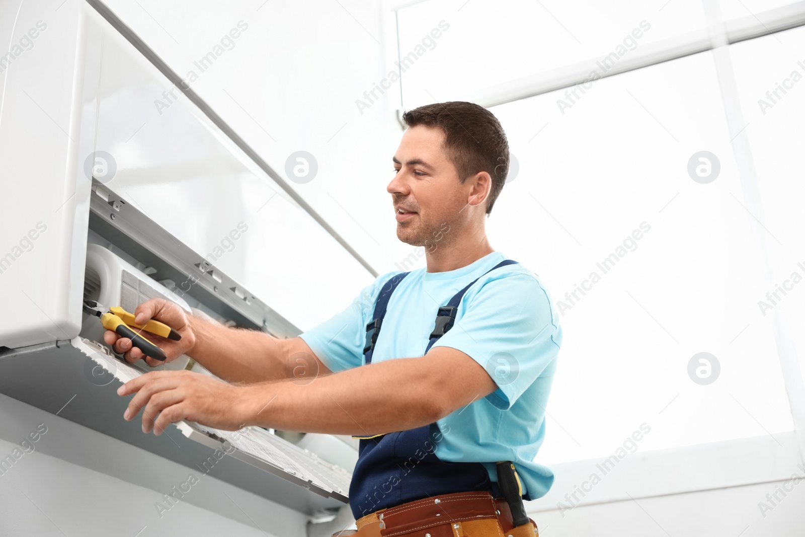 Photo of Male technician repairing modern air conditioner indoors