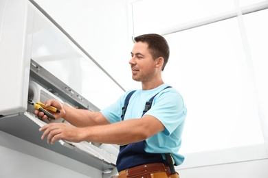 Photo of Male technician repairing modern air conditioner indoors