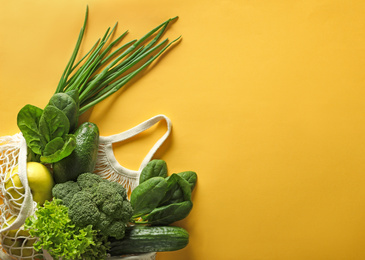 Net bag with vegetables and fruits on yellow background, flat lay. Space for text