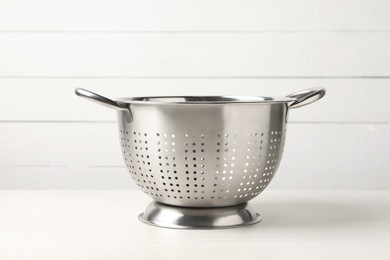 Photo of One metal colander on white wooden table