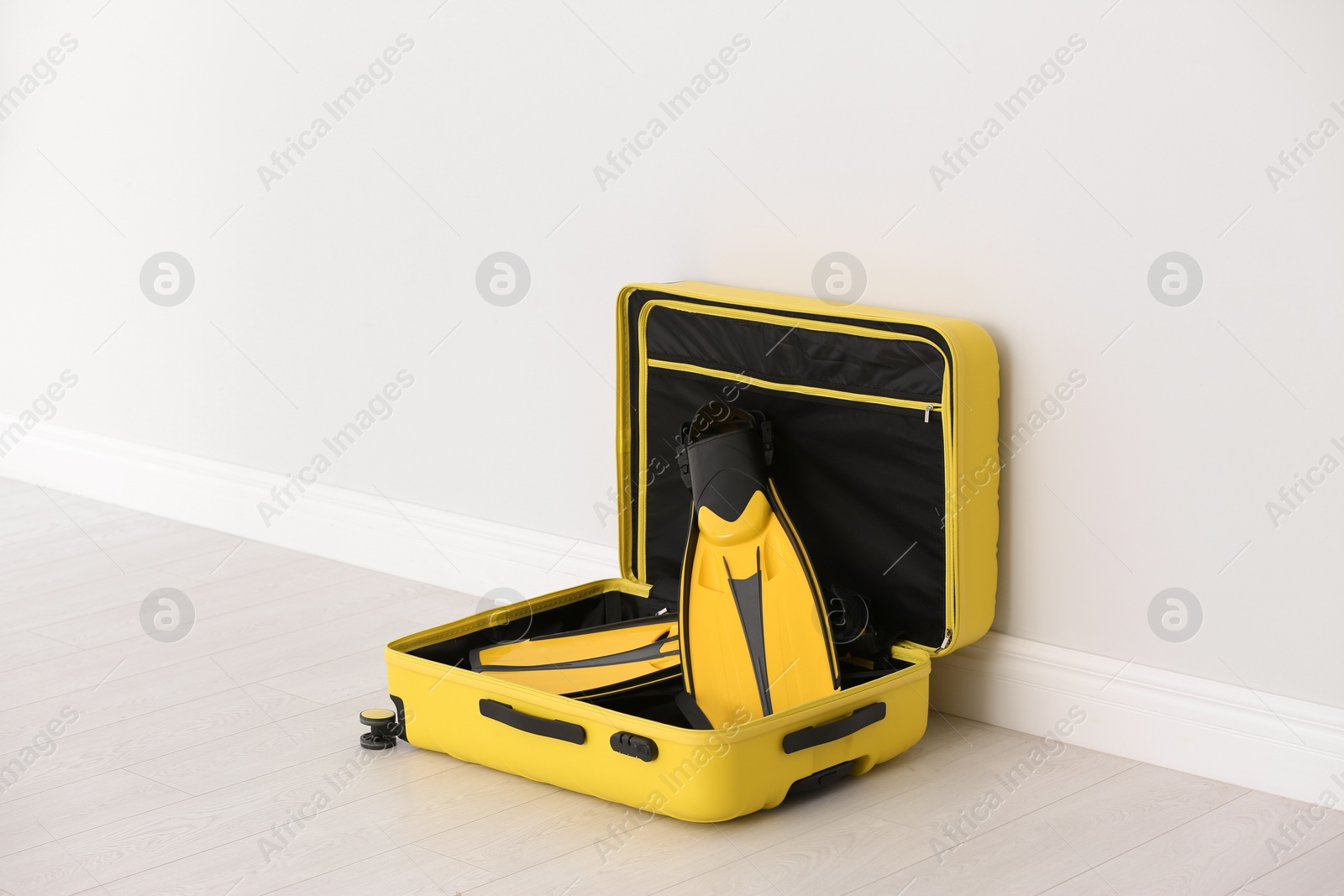 Photo of Modern suitcase with flippers on floor near light wall