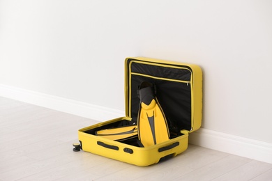 Photo of Modern suitcase with flippers on floor near light wall