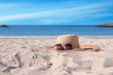 Photo of Straw hat with sunglasses on sandy beach. Space for text