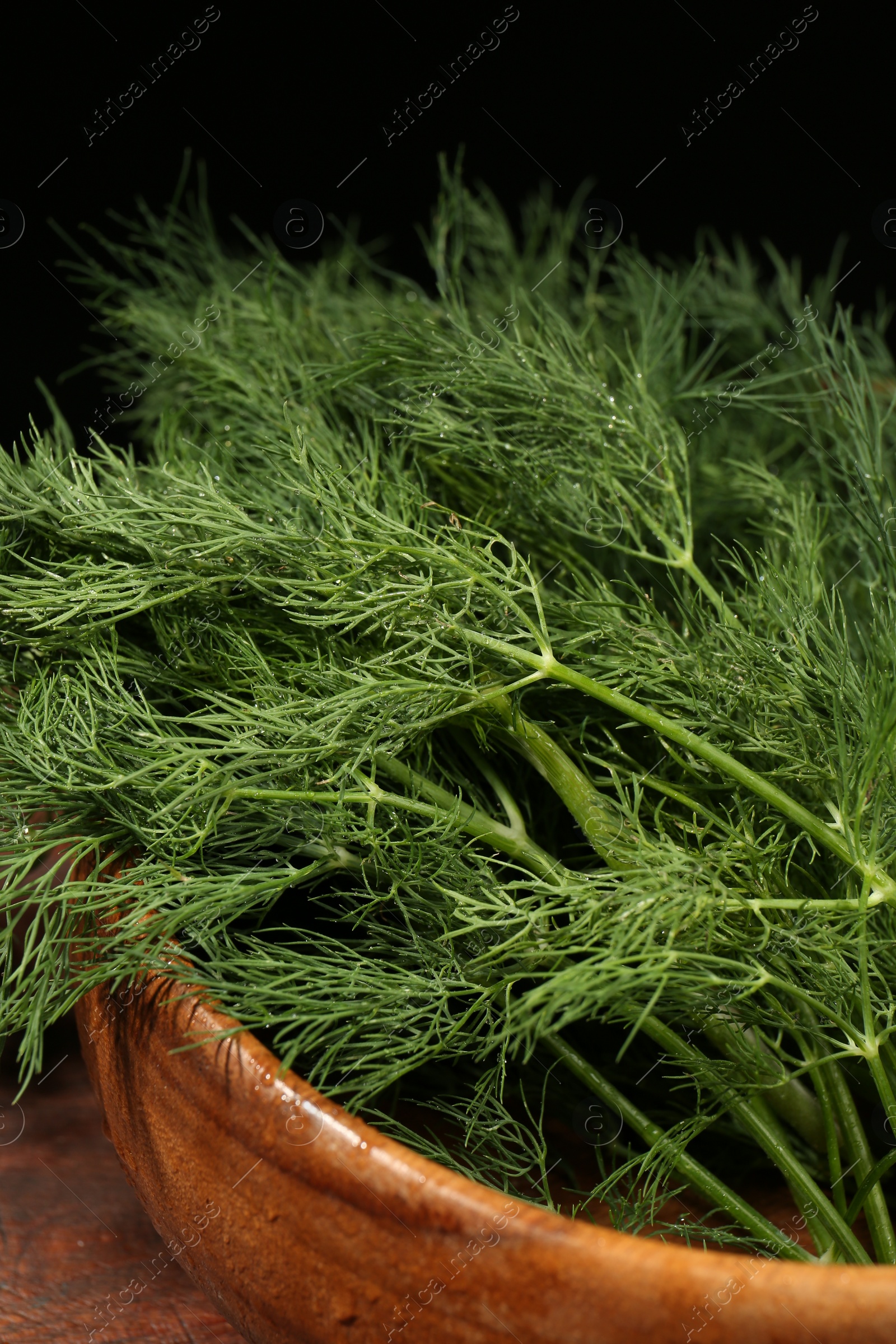 Photo of Wooden bowl of fresh green dill with water drops on table against black background, closeup