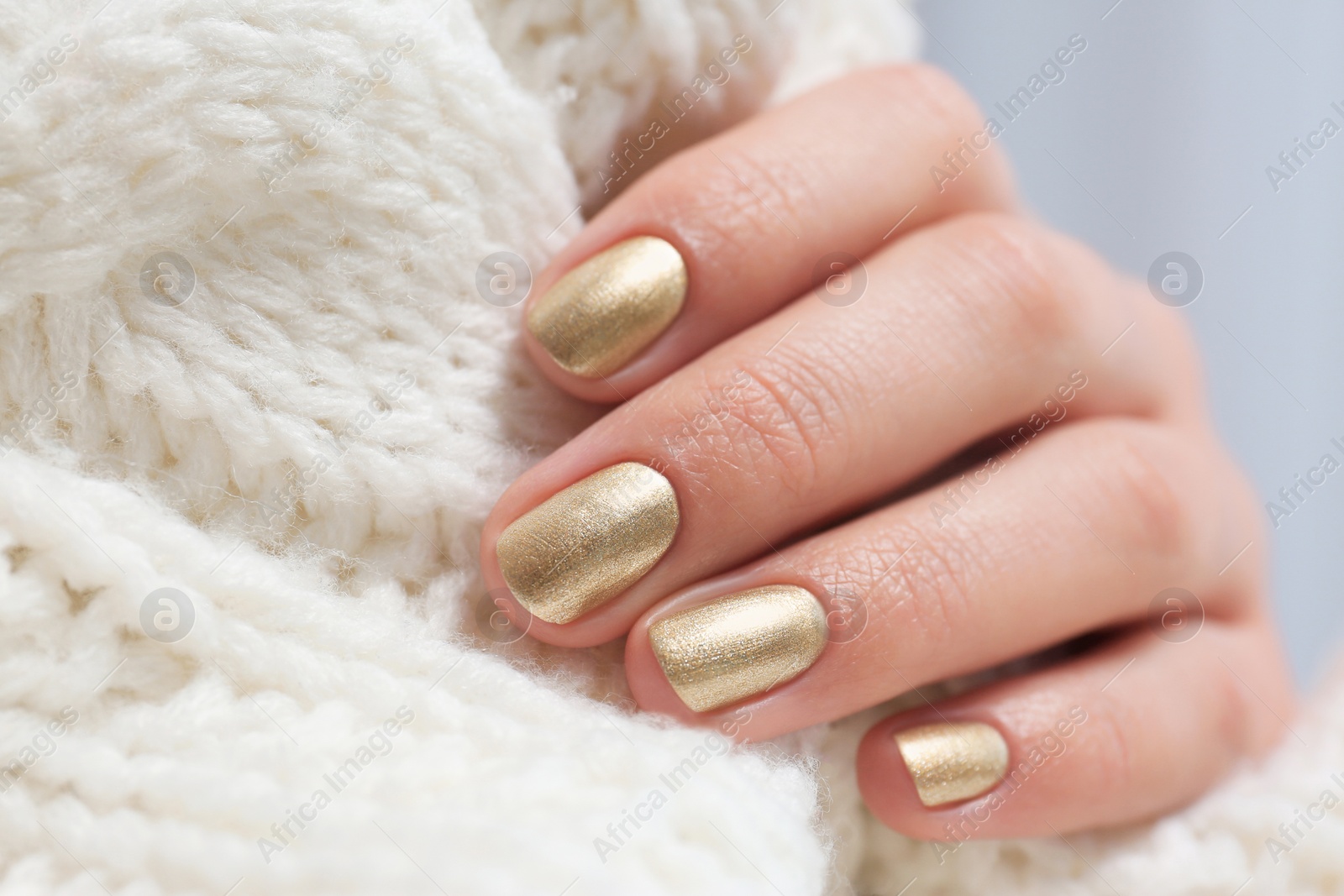 Photo of Woman with golden manicure holding knitted fabric, closeup. Nail polish trends