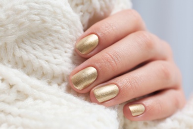 Photo of Woman with golden manicure holding knitted fabric, closeup. Nail polish trends