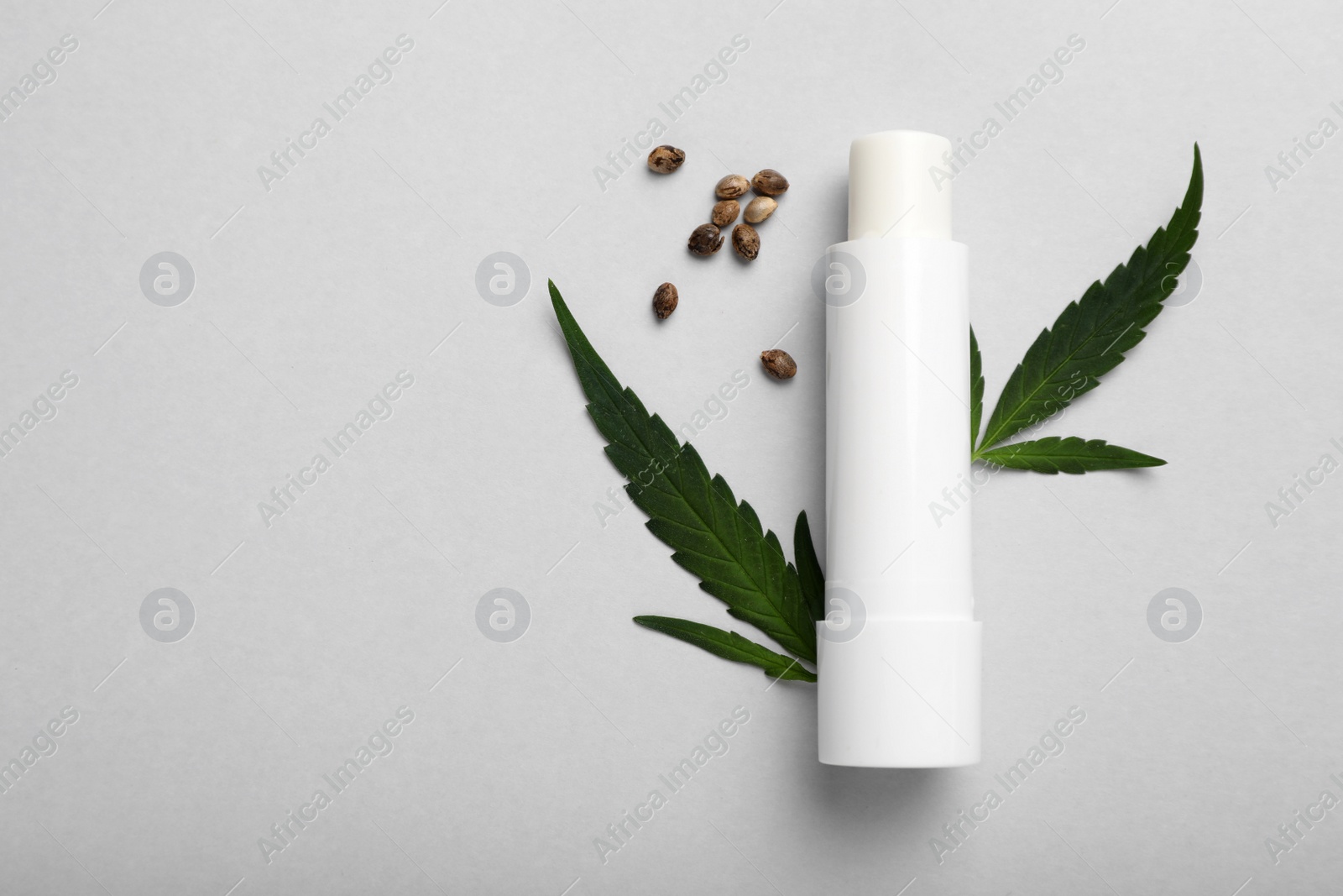 Photo of Hygienic hemp lipstick, green leaves and seeds on white background, flat lay with space for text. Natural cosmetics