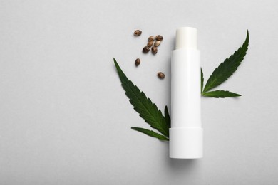 Photo of Hygienic hemp lipstick, green leaves and seeds on white background, flat lay with space for text. Natural cosmetics