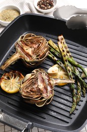 Tasty grilled artichokes, asparagus and slices of lemon on table, closeup