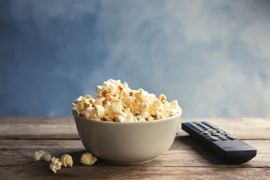 Photo of Bowl of popcorn and TV remote on table against color background. Watching cinema