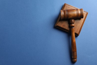 Photo of Wooden gavel and sound block on blue table, top view. Space for text