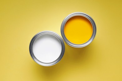 Cans with different paints on yellow background, flat lay