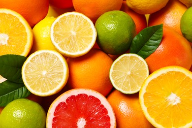 Photo of Different fresh citrus fruits and leaves as background, top view