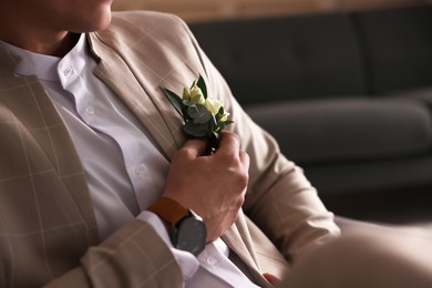 Groom wearing elegant suit and beautiful boutonniere indoors, closeup view