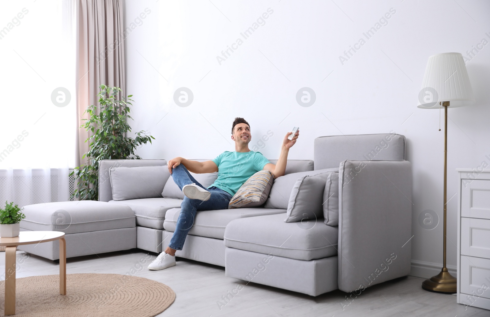 Photo of Young man with air conditioner remote control relaxing on sofa at home