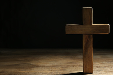 Photo of Christian cross on wooden table against black background, space for text. Religion concept