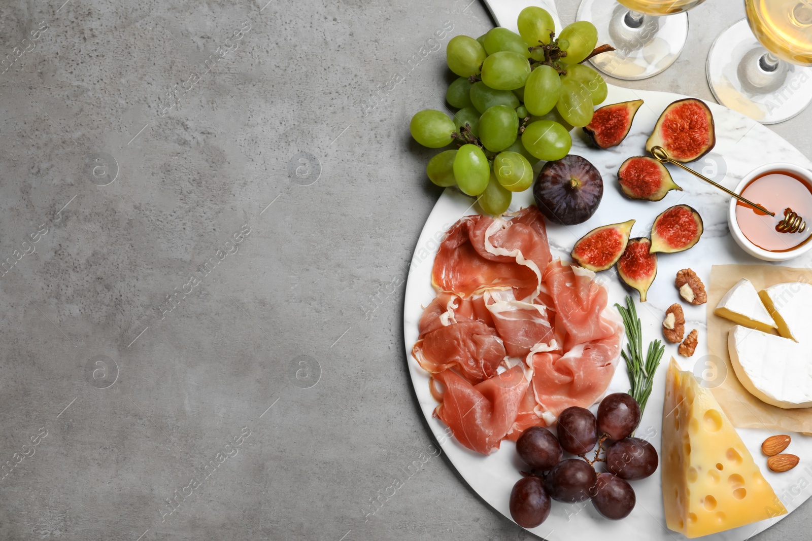 Photo of Delicious ripe figs, prosciutto and cheeses served on grey table, flat lay. Space for text