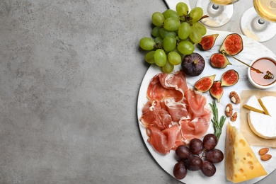 Delicious ripe figs, prosciutto and cheeses served on grey table, flat lay. Space for text