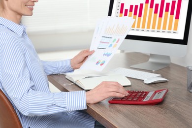 Professional accountant using calculator at wooden desk in office, closeup