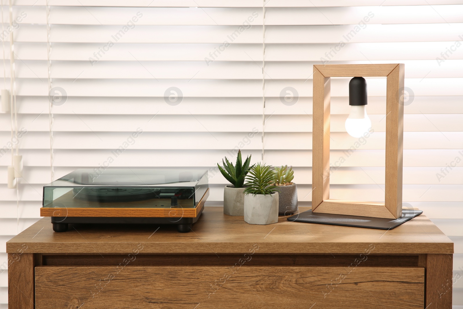 Photo of Stylish turntable with vinyl record on wooden chest of drawers indoors