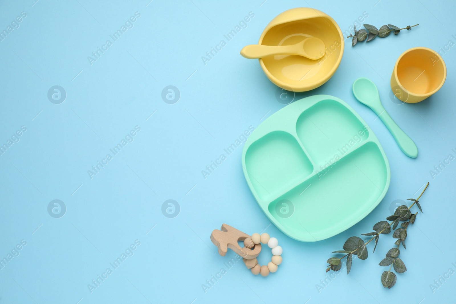 Photo of Set of plastic dishware and wooden toy on light blue background, flat lay with space for text. Serving baby food