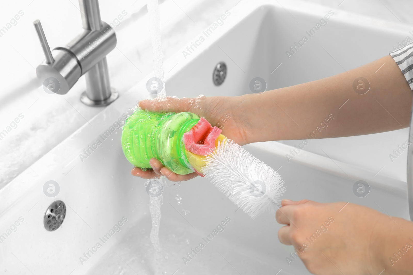 Photo of Woman washing baby bottle under stream of water in kitchen, closeup