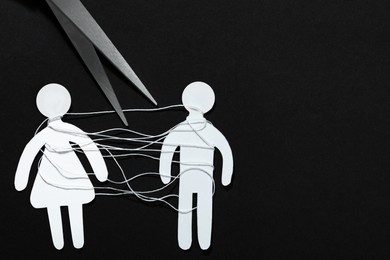 Photo of Divorce concept. Paper human figures with white thread and scissors on black background, flat lay. Space for text