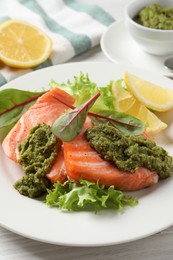 Photo of Tasty cooked salmon with pesto sauce served on white wooden table, closeup