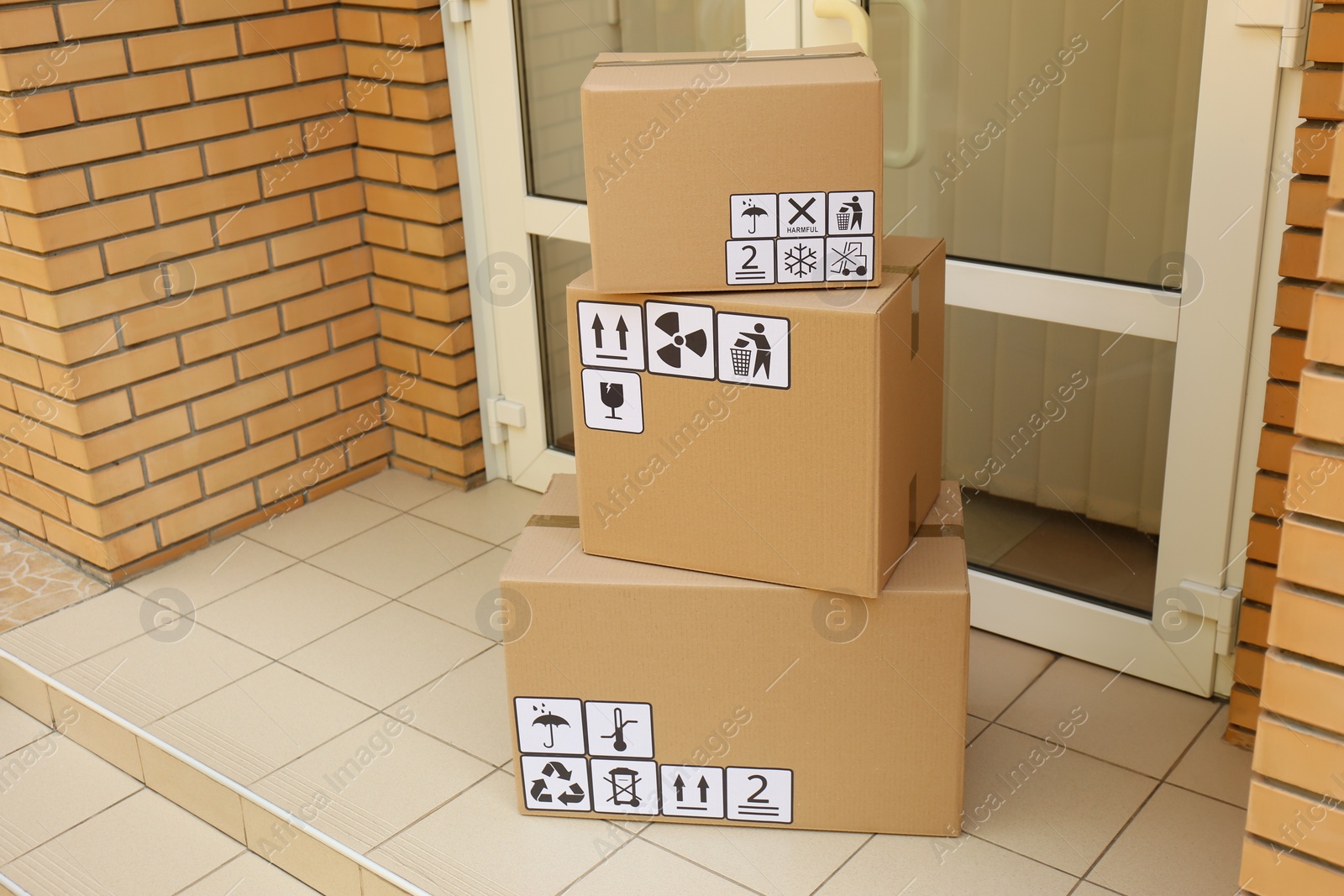 Photo of Cardboard boxes with different packaging symbols on floor near entrance. Parcel delivery