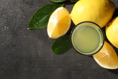 Photo of Tasty limoncello liqueur, lemons and green leaves on grey table, top view. Space for text