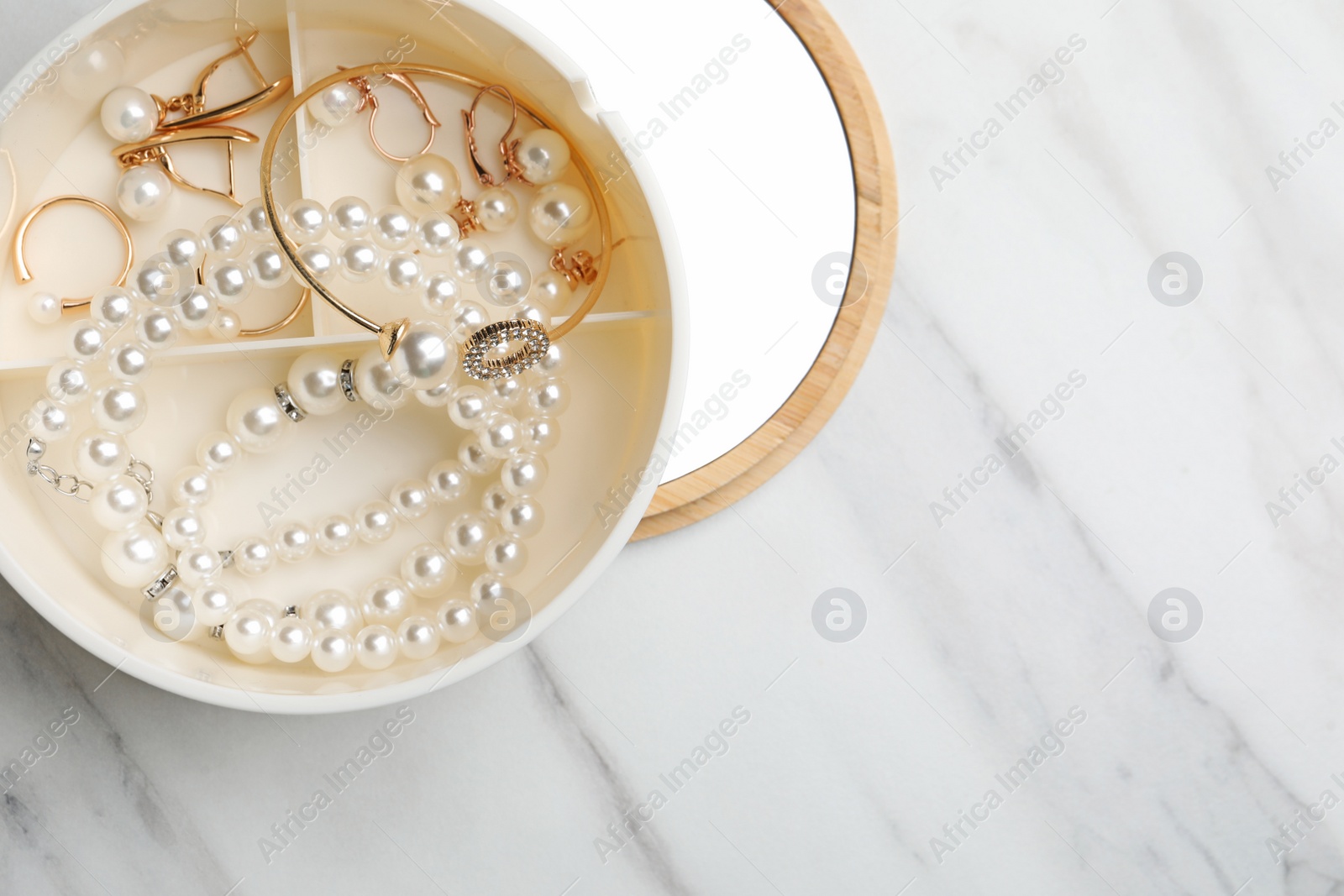 Photo of Stylish jewelry with pearls in box on white marble table, top view. Space for text