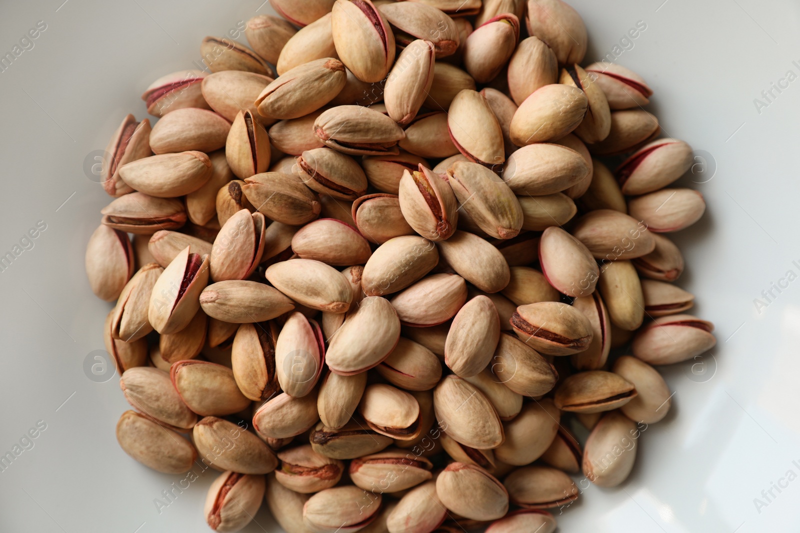 Photo of Many tasty pistachios on plate, top view