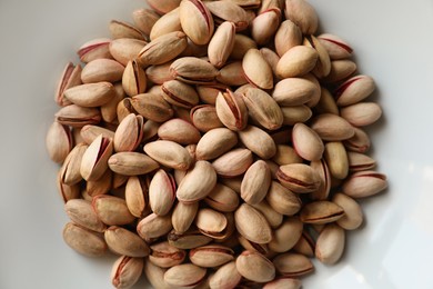 Many tasty pistachios on plate, top view