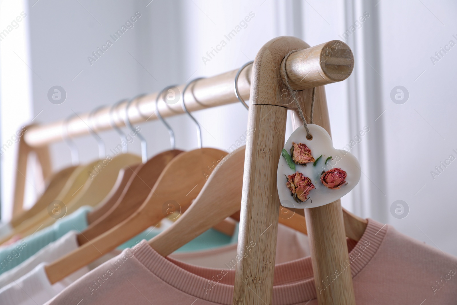 Photo of Beautiful heart shaped scented wax sachet and clothes hanging on wooden rack indoors, closeup