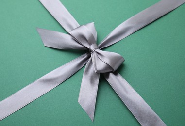 Photo of Grey satin ribbon with bow on green background, closeup