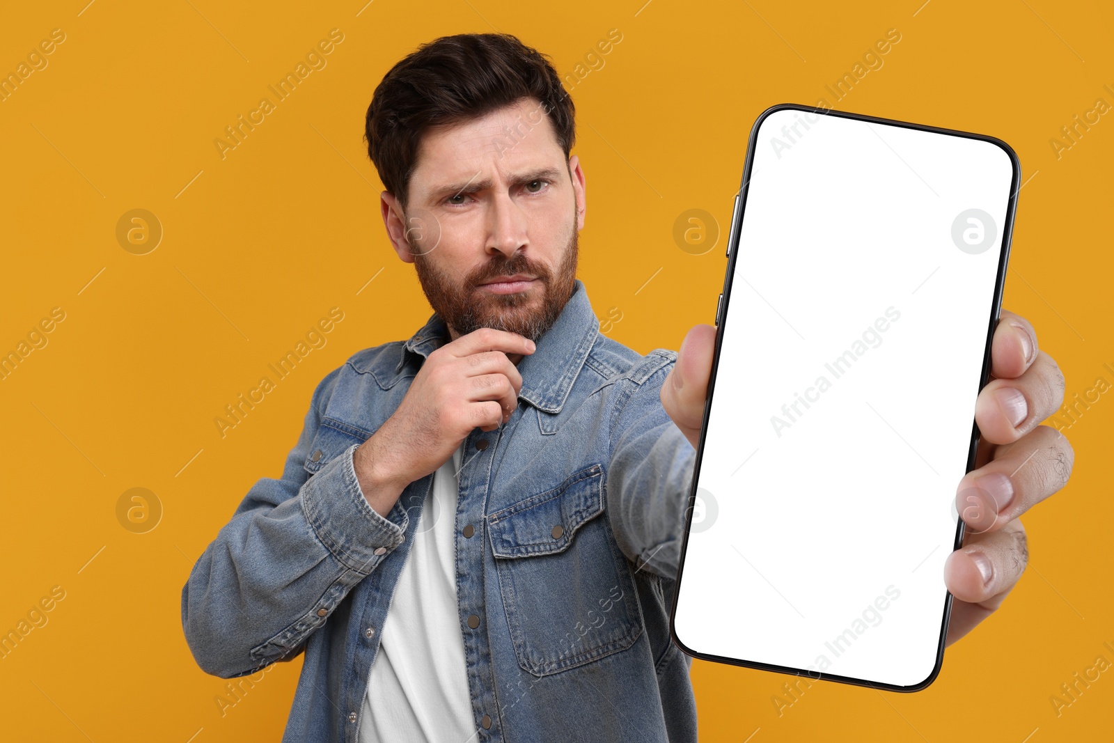 Image of Man holding smartphone with empty screen on orange background