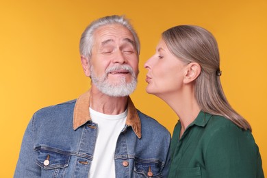Photo of Senior woman kissing her beloved man on orange background