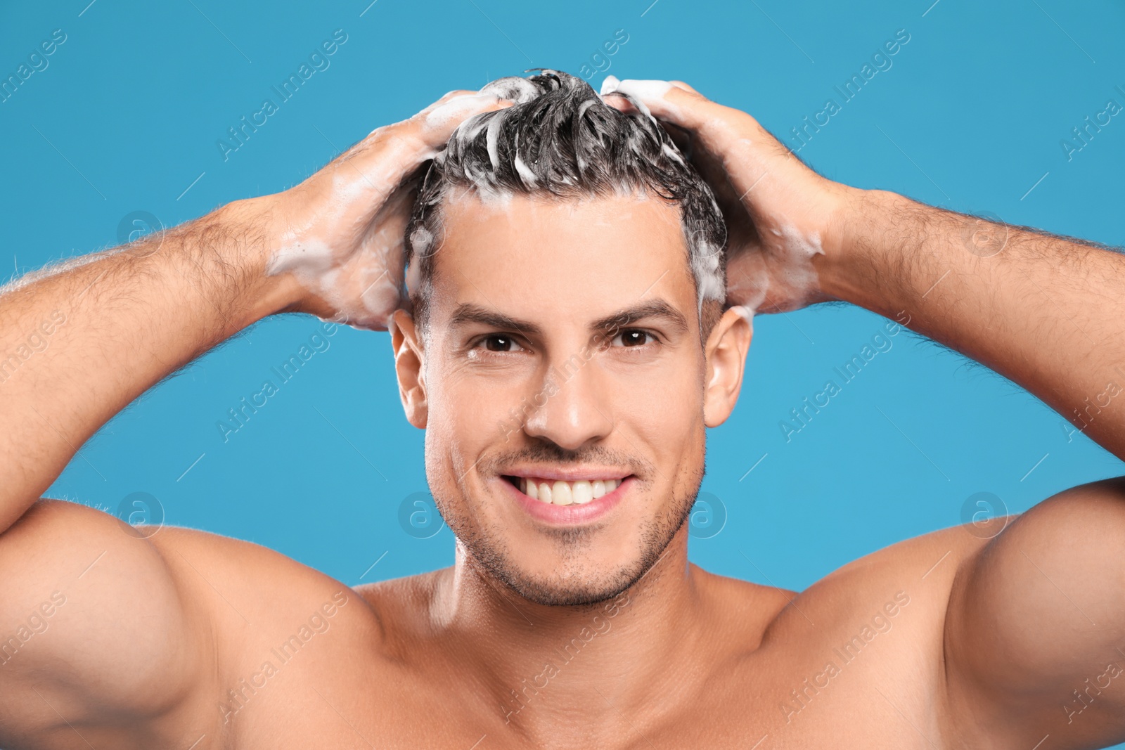 Photo of Handsome man washing hair on light blue background