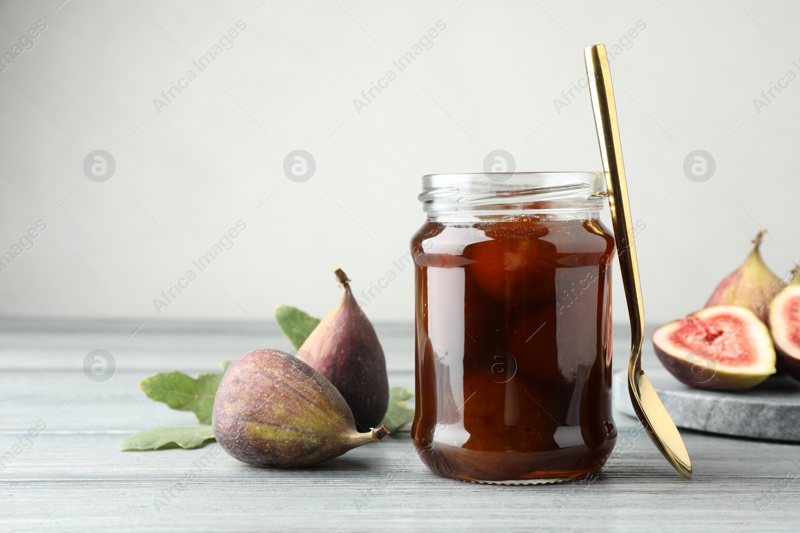 Photo of Jar of tasty sweet jam and fresh figs on grey table