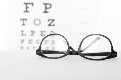Photo of Glasses with corrective lenses on table against eye chart