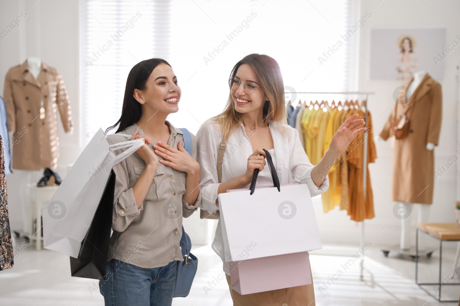 Photo of Young women with shopping bags choosing clothes in modern boutique