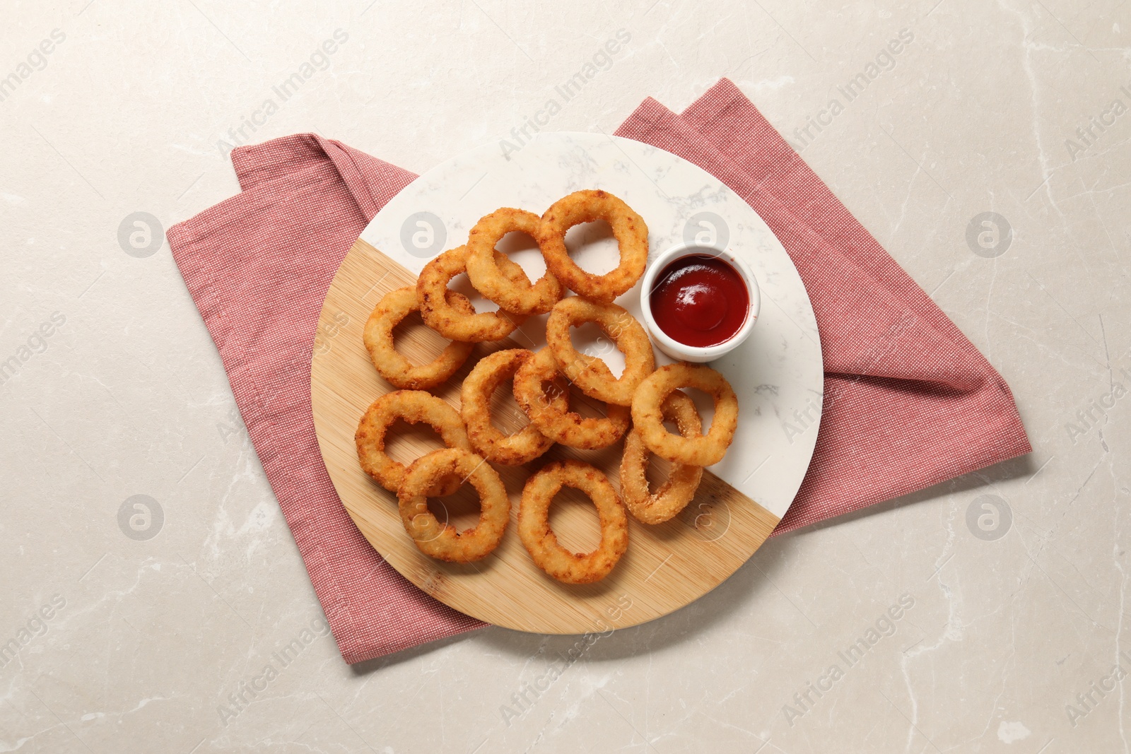 Photo of Board with tasty ketchup and onion rings on marble table, top view