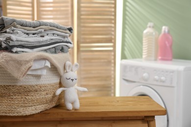 Photo of Laundry basket with baby clothes and toy on table in bathroom, closeup. Space for text