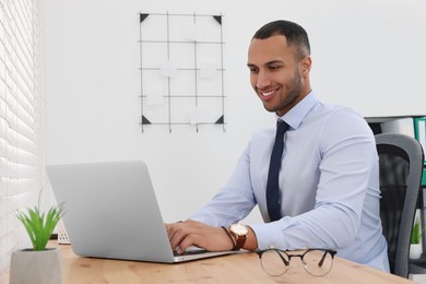 Photo of Happy young intern working with laptop at table in modern office