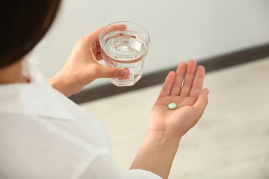Photo of Young woman with glass of water and dietary supplement pill indoors, closeup