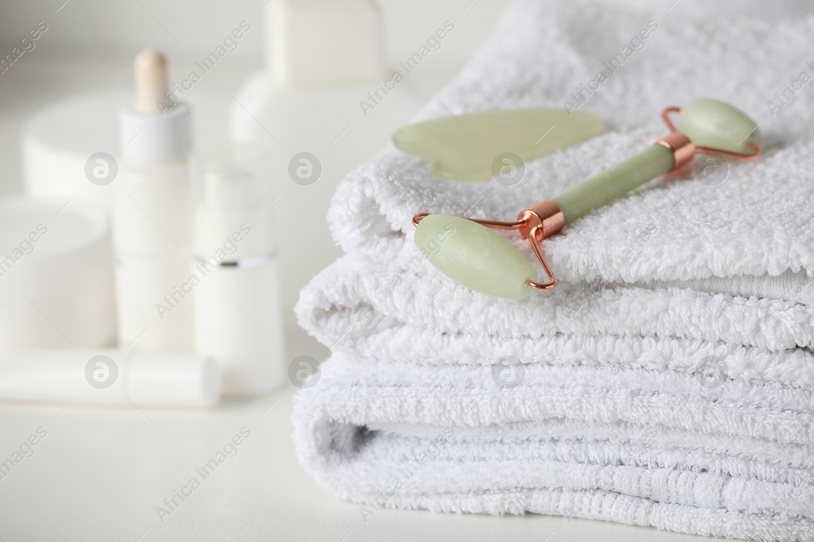 Photo of Natural face roller, gua sha tool and towels on white table, closeup