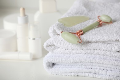 Photo of Natural face roller, gua sha tool and towels on white table, closeup