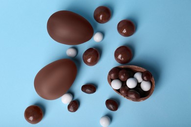 Photo of Tasty chocolate eggs and different sweets on light blue background, flat lay