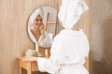 Photo of Beautiful woman wearing white bathrobe in front of mirror at home